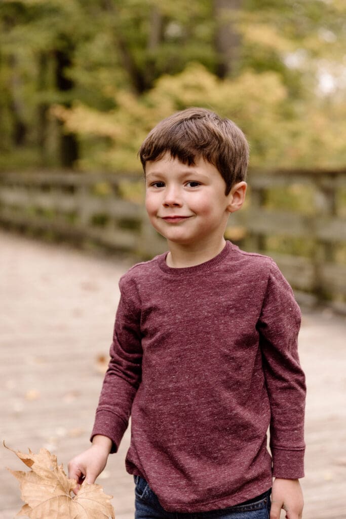 Boy holding a leaf and smiling at the camera.