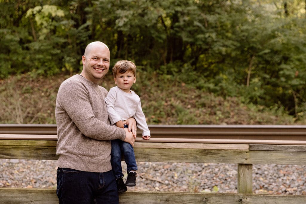 Dad holding son on a wooden railing.