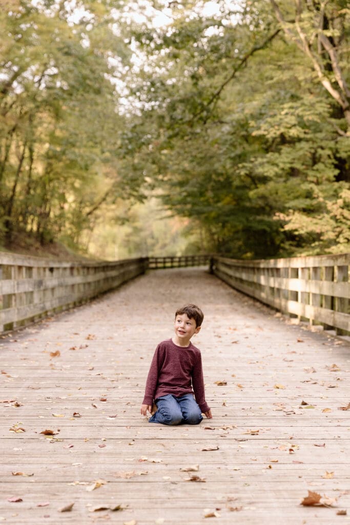 Boy sitting in the middle of a wooden trail.