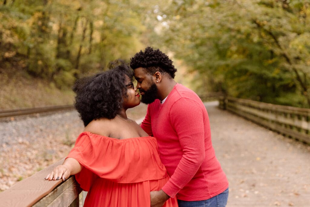 Couple embracing while leaning against a wooden rail.