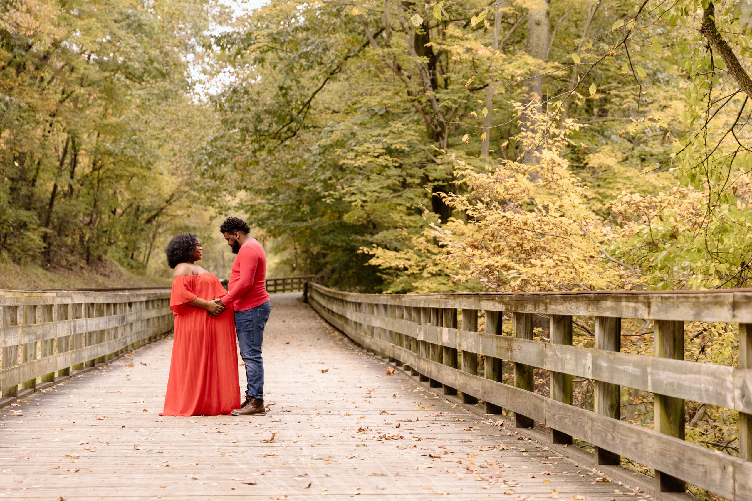 Maternity couple facing each other in a park.